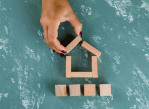 real-estate-concept-with-wooden-blocks-flat-lay-woman-making-house-model